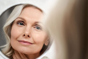 An older woman with incredibly smooth skin looking into a mirror and smiling